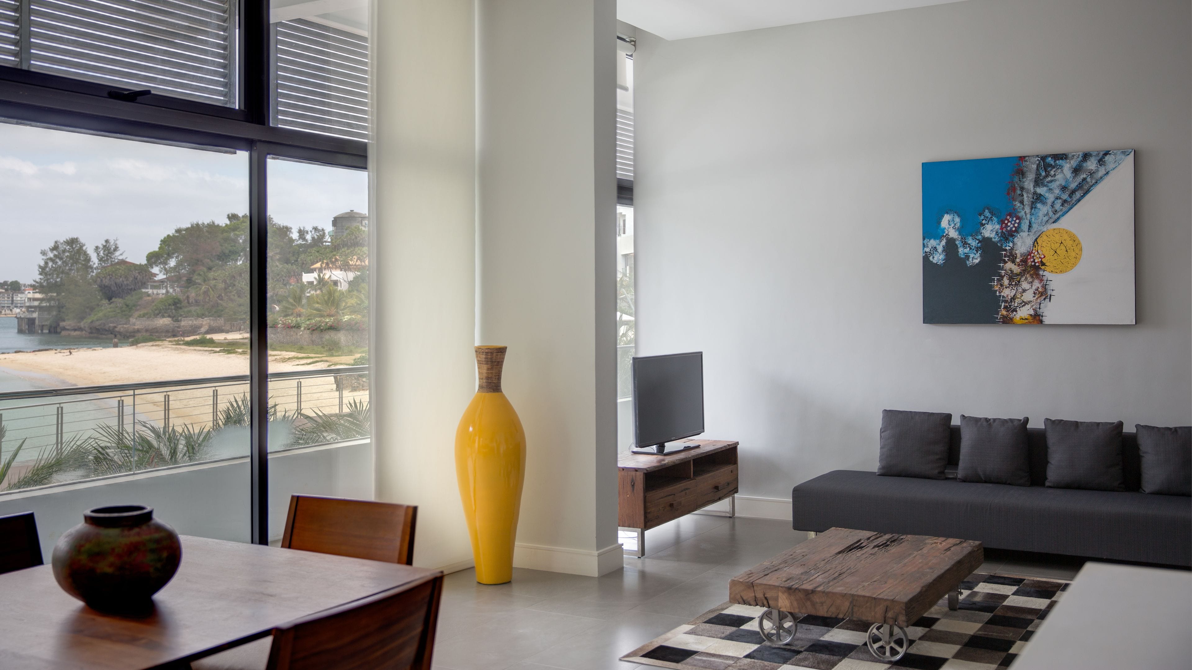 A modern living room with a large window, a sofa, a TV, and a yellow vase.