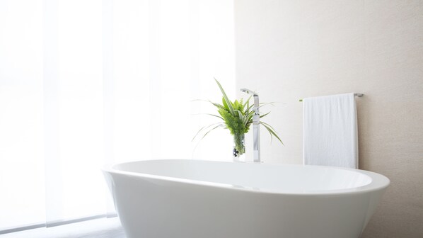 Un baño moderno con una bañera independiente, un florero de vidrio con plantas verdes y una toalla blanca colgada en un perchero.