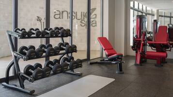 Un gimnasio con equipo de levantamiento de pesas, una banca roja y una pared con la marca 'anSuna Spa'.