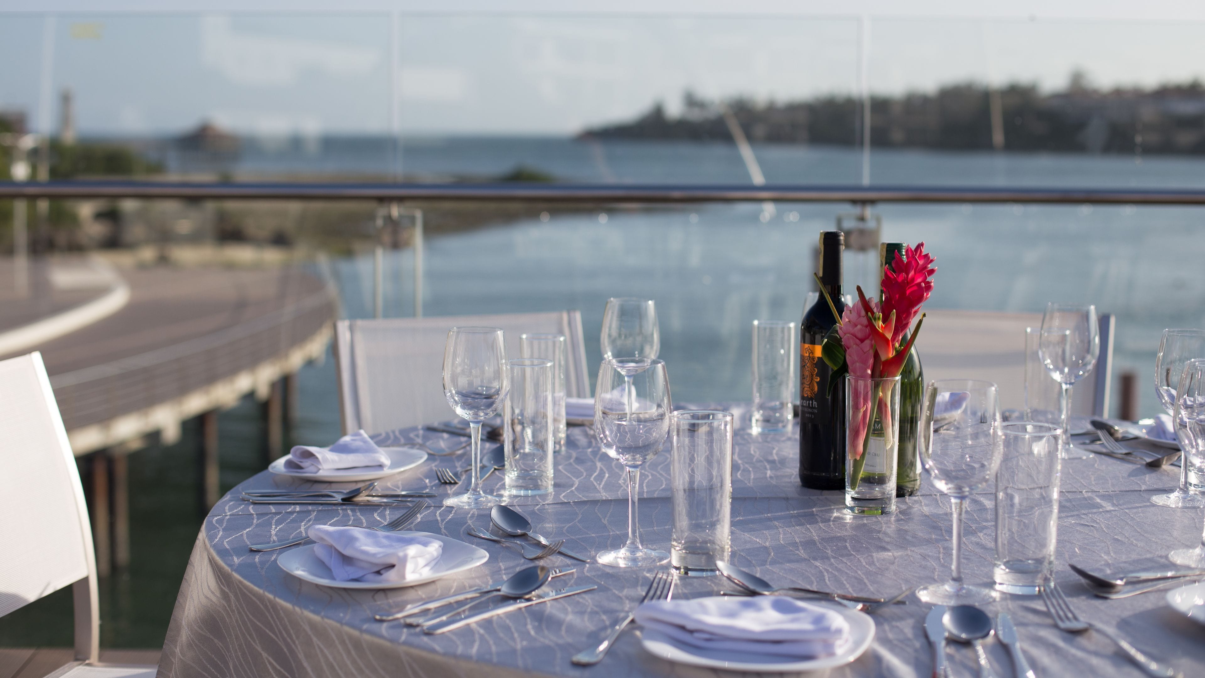 Una mesa preparada para comer con vista al mar y un muelle al fondo.