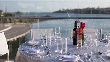 Una mesa preparada para comer con vista al mar y un muelle al fondo.