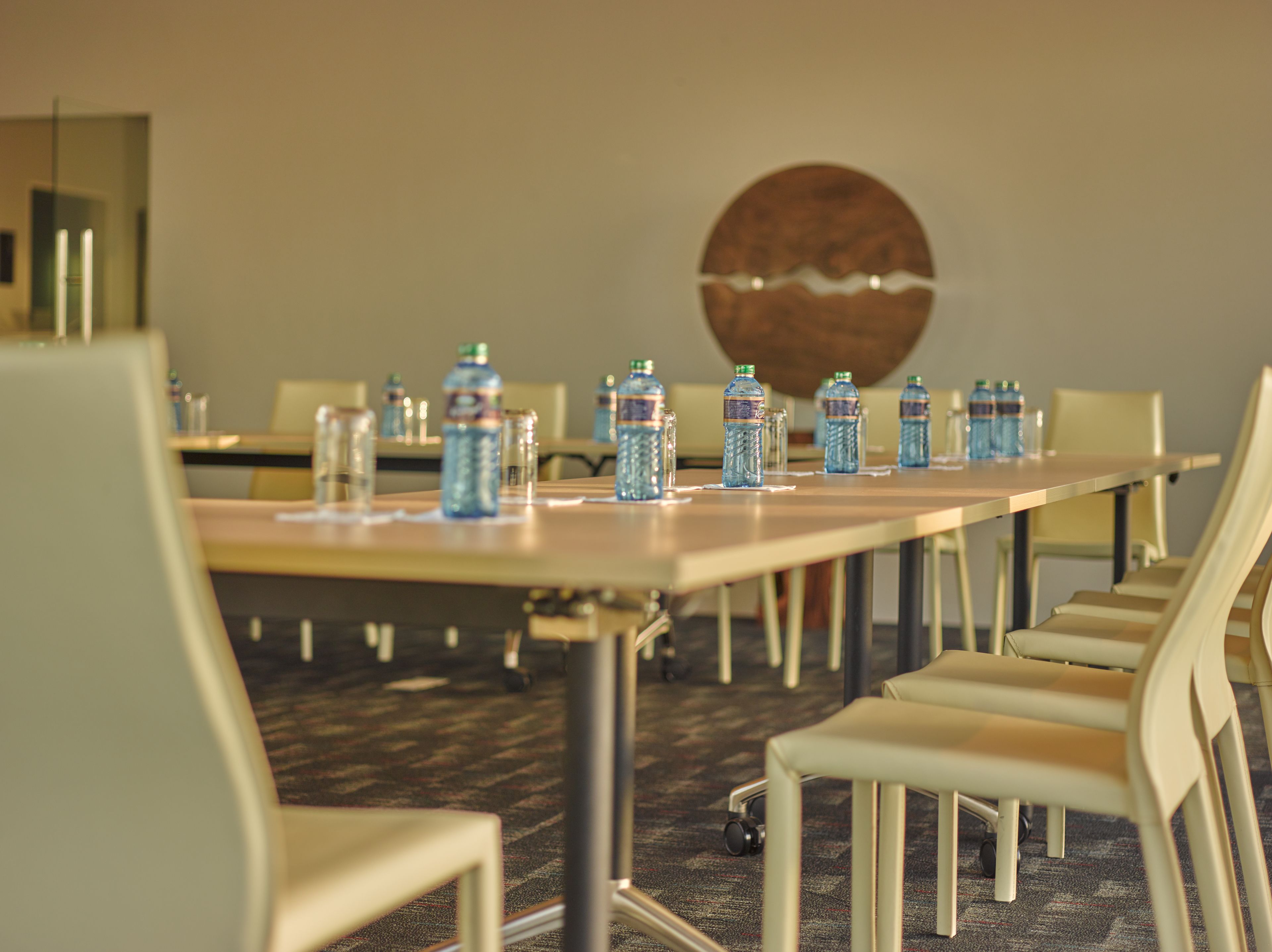 A conference room with a long table, chairs, water bottles, and a round wall decoration.