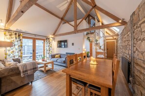 A spacious living room with a wooden dining table, a sofa, and a staircase leading to an upper level. - Somerset Country Escape (Taunton)