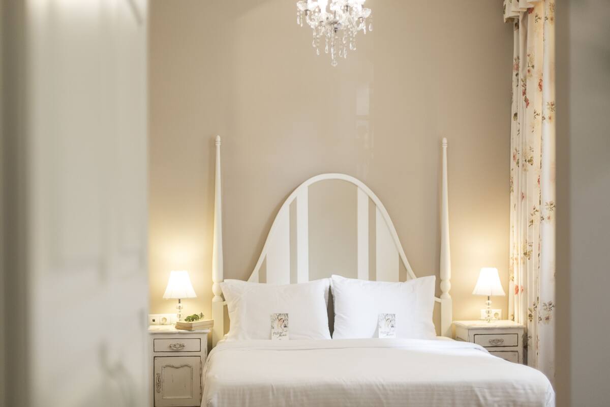 A neatly made bed with white linens and a white headboard, flanked by two bedside tables with lamps.