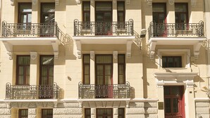 Un edificio de varios pisos con balcones y un coche rojo estacionado adelante.