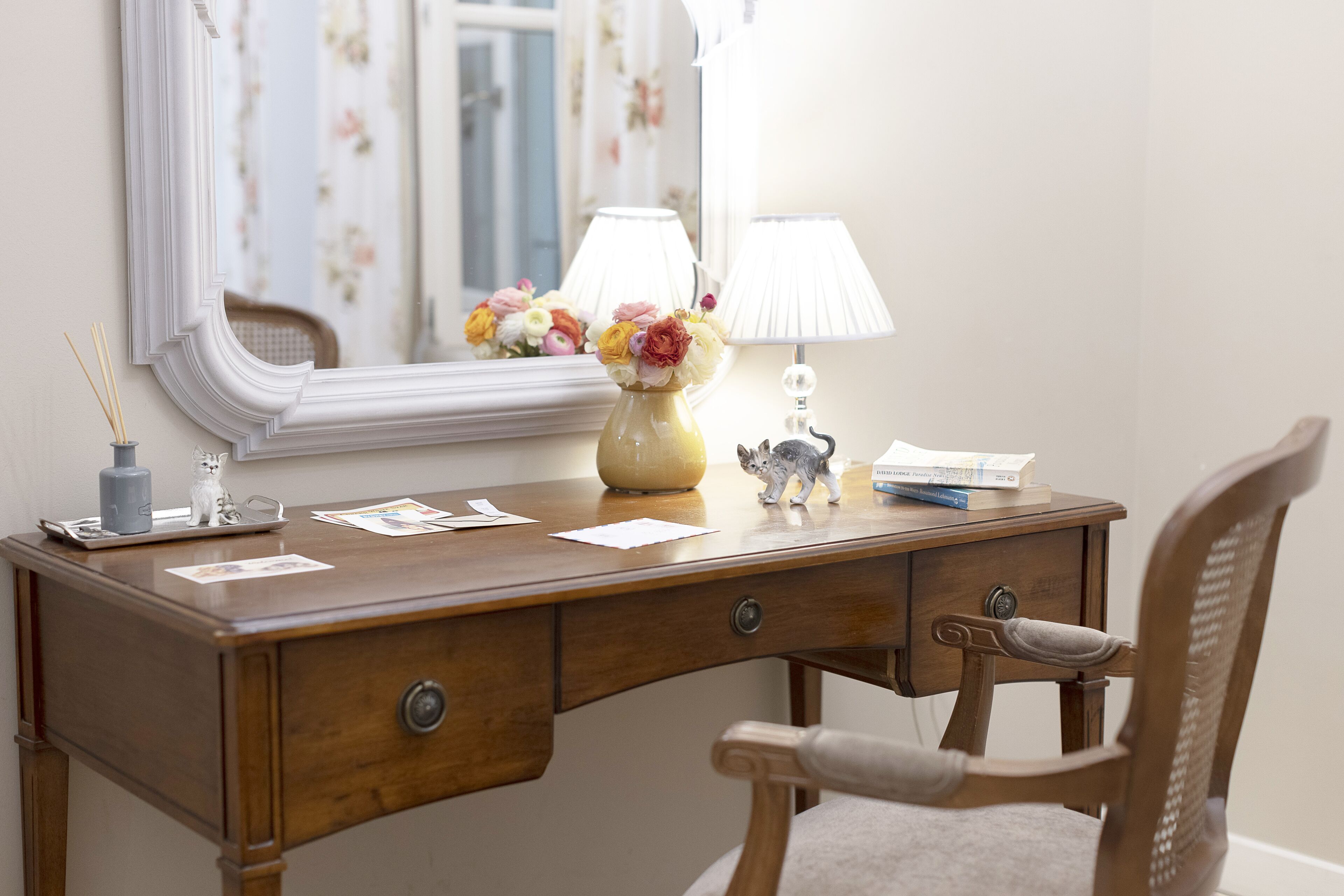 Un bureau en bois orné d’un vase de fleurs, d’une lampe et d’une petite figurine.