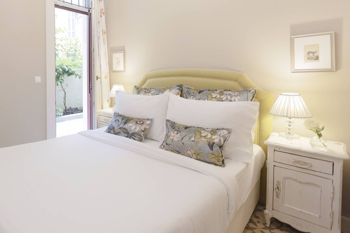 A neatly made bed with floral-patterned pillows, a bedside table with a lamp, and a framed picture on the wall.