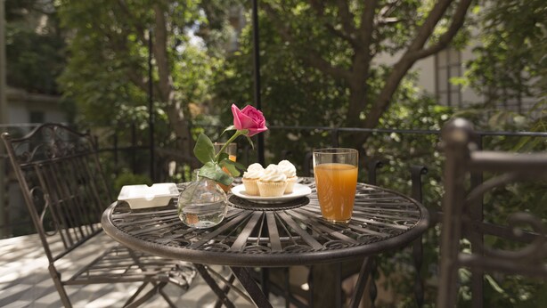 Una mesa metálica redonda con una rosa, cupcakes y un vaso de jugo de naranja.
