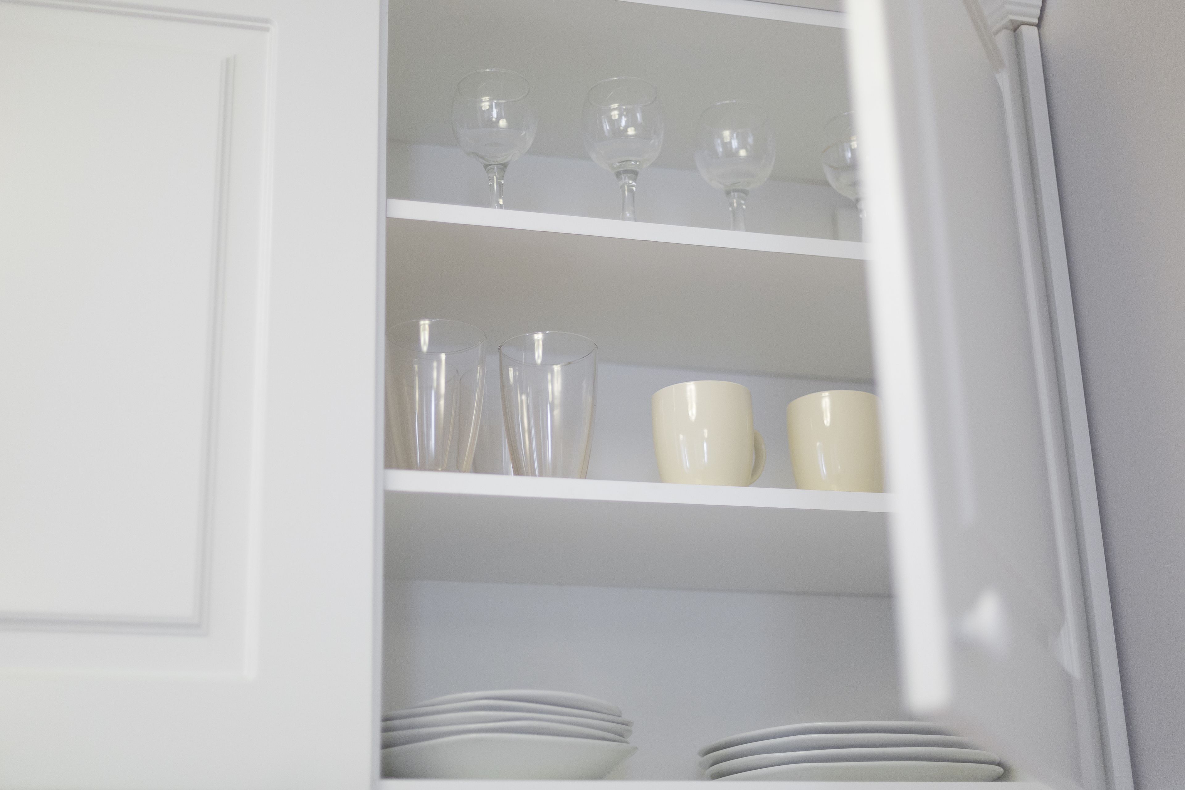 Interior blanco con estantes que exhiben vasos transparentes, platos blancos y una taza blanca.