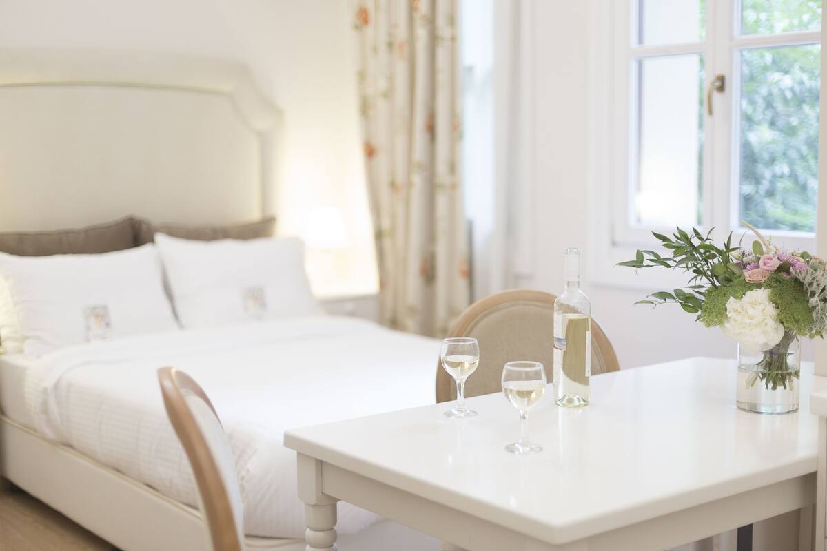 A neatly made bed with white linens, a bedside table with two glasses of water, and a vase with flowers.