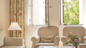 Una habitación con un sofá color beige, un sillón a juego, una mesita con una lámpara y una ventana con cortinas.