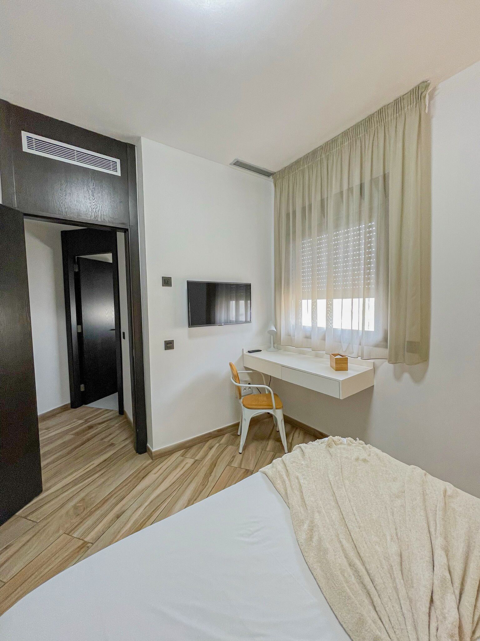A hotel room with a bed, a desk with a chair, a TV, and a window with curtains.