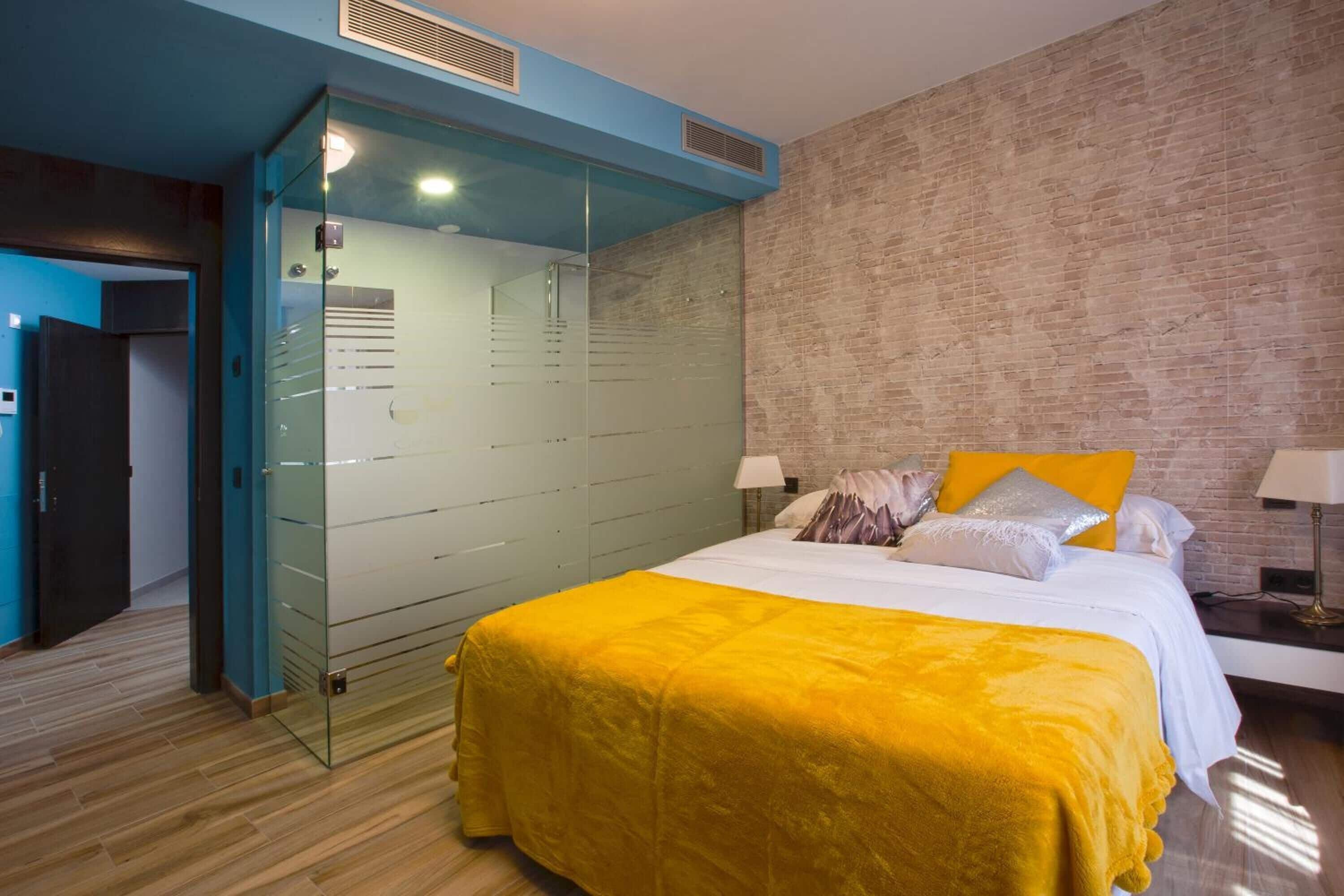 Une chambre d’hôtel moderne avec un grand lit, une cloison en verre et un mur en briques.