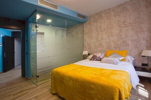 Une chambre d’hôtel moderne avec un grand lit, une cloison en verre et un mur en briques.