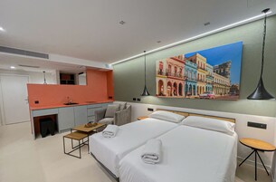 A hotel room with a bed, a desk, a chair, a small table, and a painting on the wall.