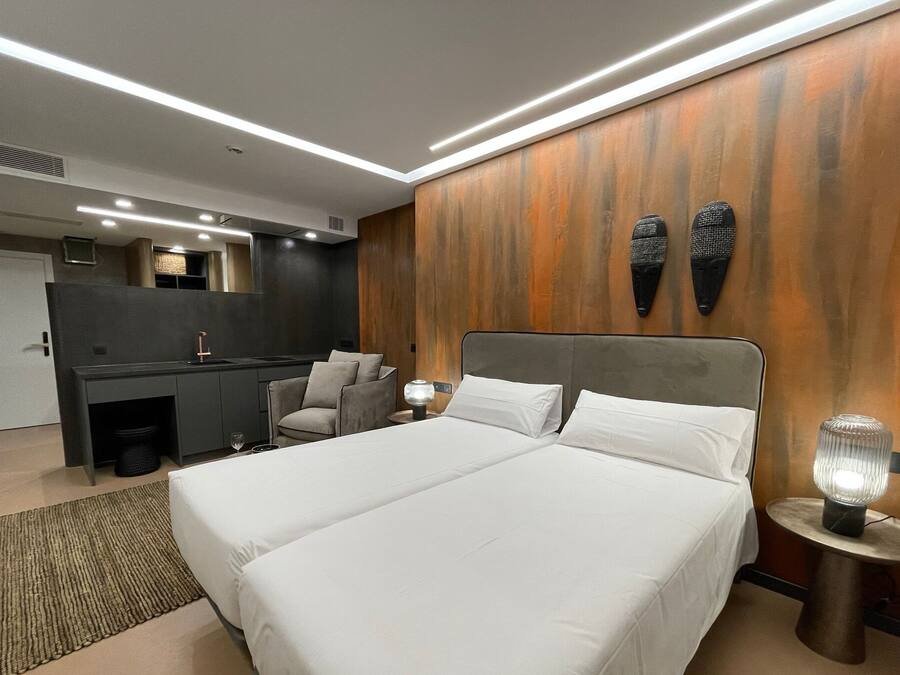 Una habitación de hotel moderna con una cama grande, un escritorio, una silla y una mesita con una lámpara.