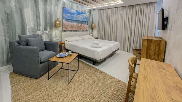 A modern hotel room with a bed, a sofa, a coffee table, and a TV. - Gran Marina Suites (Las Palmas de Gran Canaria)