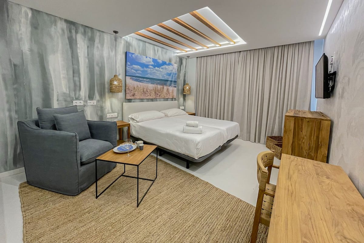 A modern hotel room with a bed, a sofa, a coffee table, and a TV.
