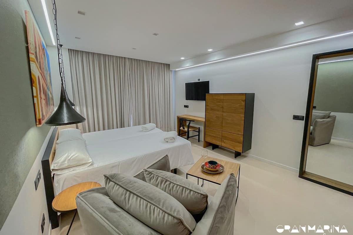 A modern hotel room with a bed, a sofa, a desk, and a wardrobe.