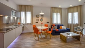 A modern living room with a blue sofa, orange chairs, a coffee table, and a kitchen area with a sink and stove. - Gran Marina Suites (Las Palmas de Gran Canaria)