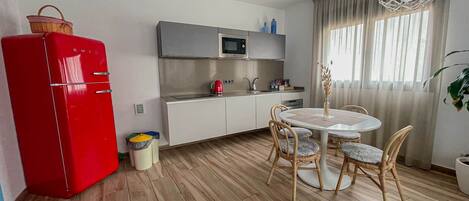 Cocina compacta con un refrigerador rojo, un microondas y un lavamanos. Hay una zona de comedor con una mesa redonda y cuatro sillas.