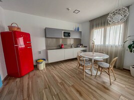 Pieni, käytännöllinen keittiö, jossa on punainen jääkaappi, mikroaaltouuni ja pesuallas. Keittiössä on myös ruokailutila, jossa on pyöreä pöytä ja neljä tuolia.