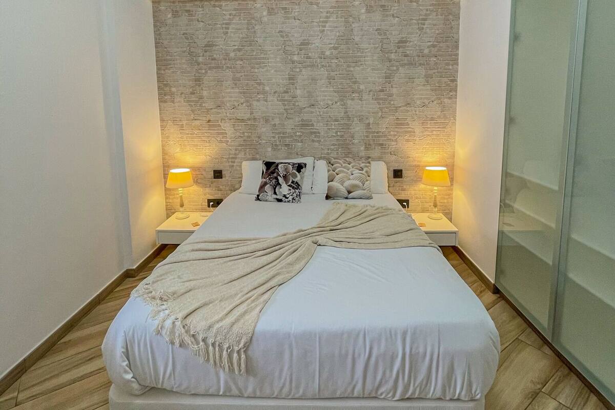 A modern bedroom with a large bed, a brick-patterned headboard, and two bedside lamps.