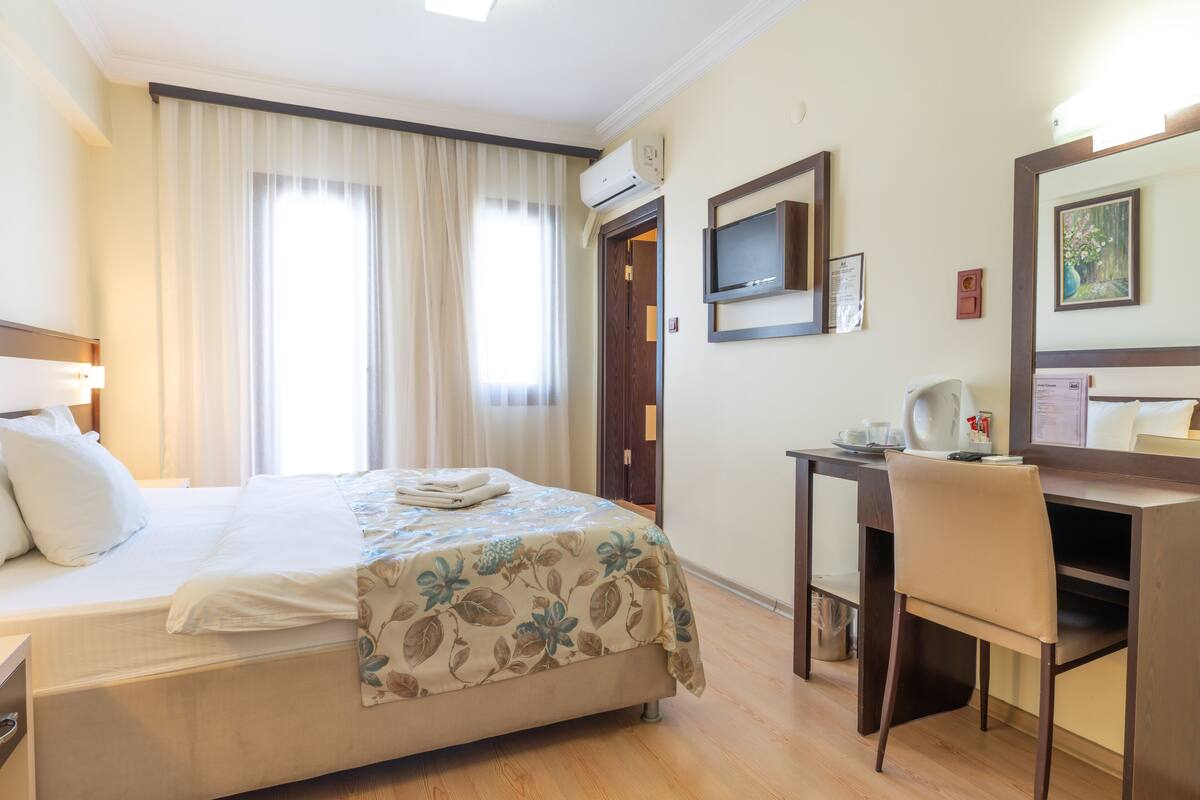 A hotel room with a bed, a desk, a chair, a television, and an air conditioning unit.