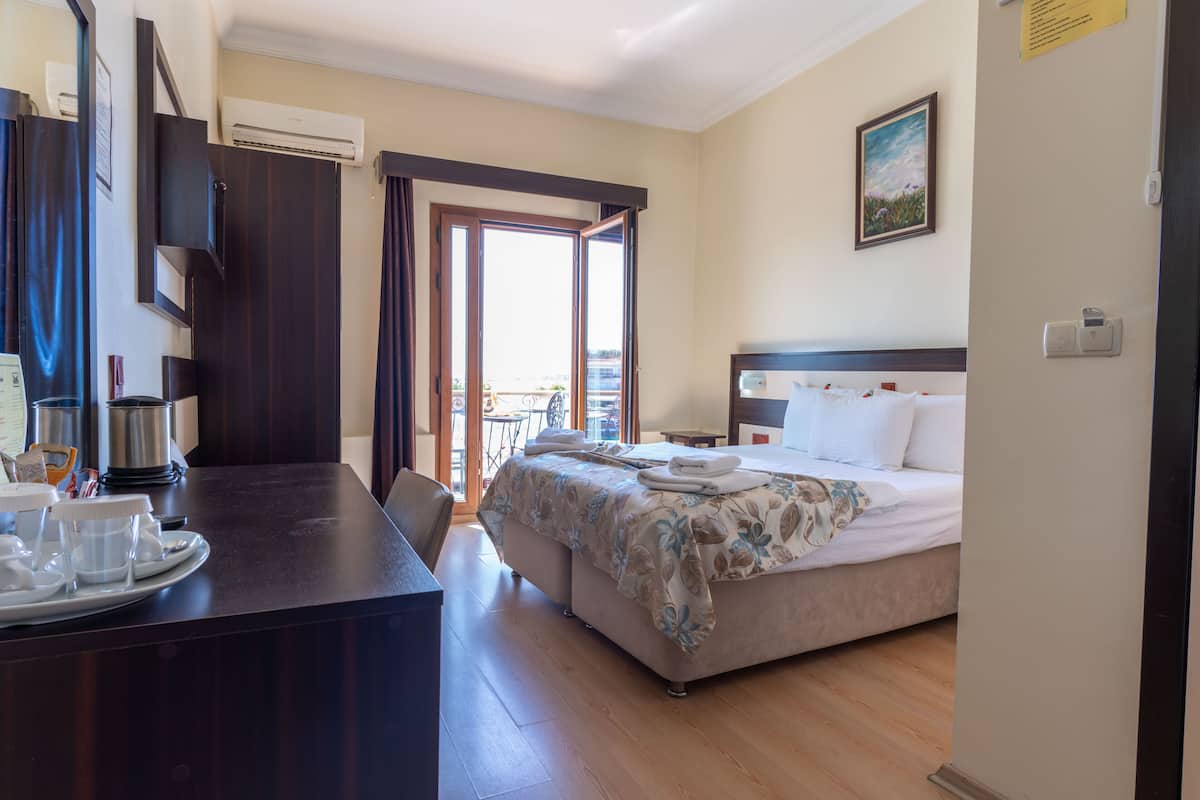 A hotel room with a bed, a desk with a coffee maker, a dining table, and a balcony view.