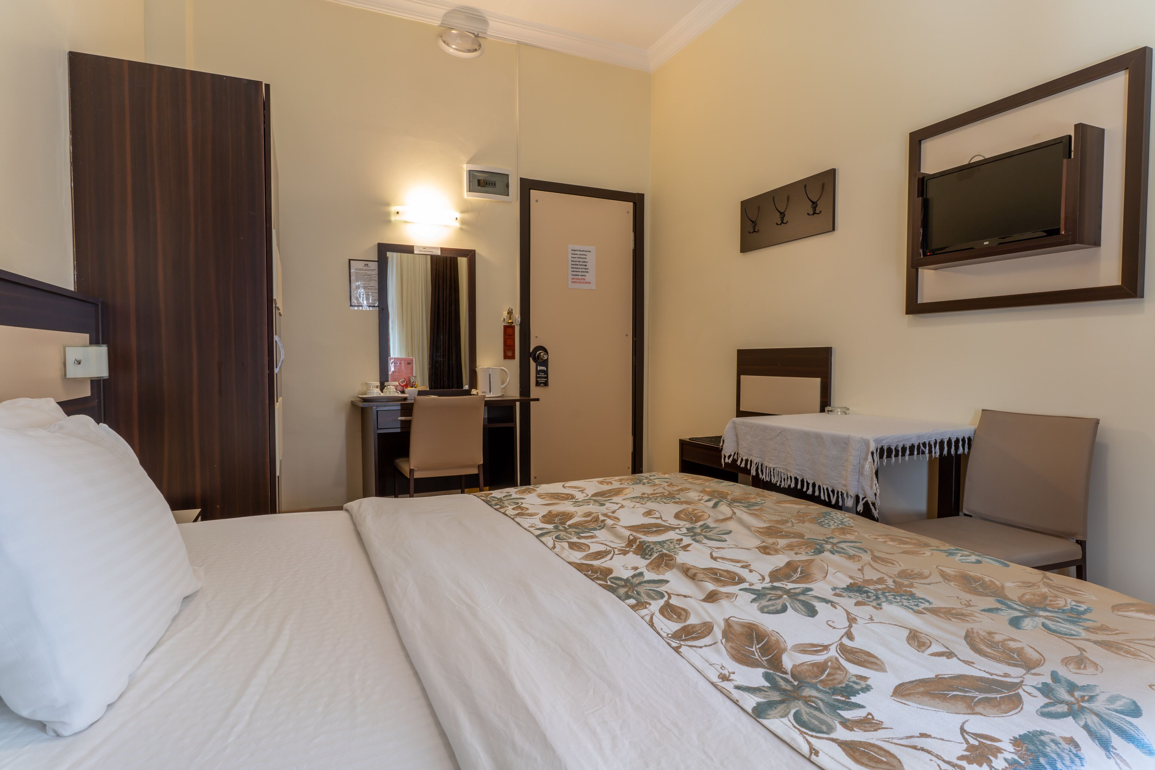 A hotel room with a bed, a desk, a chair, a mirror, a television, and a door.