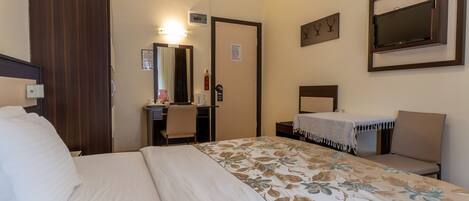 A hotel room with a bed, a desk, a chair, a mirror, a television, and a door.
