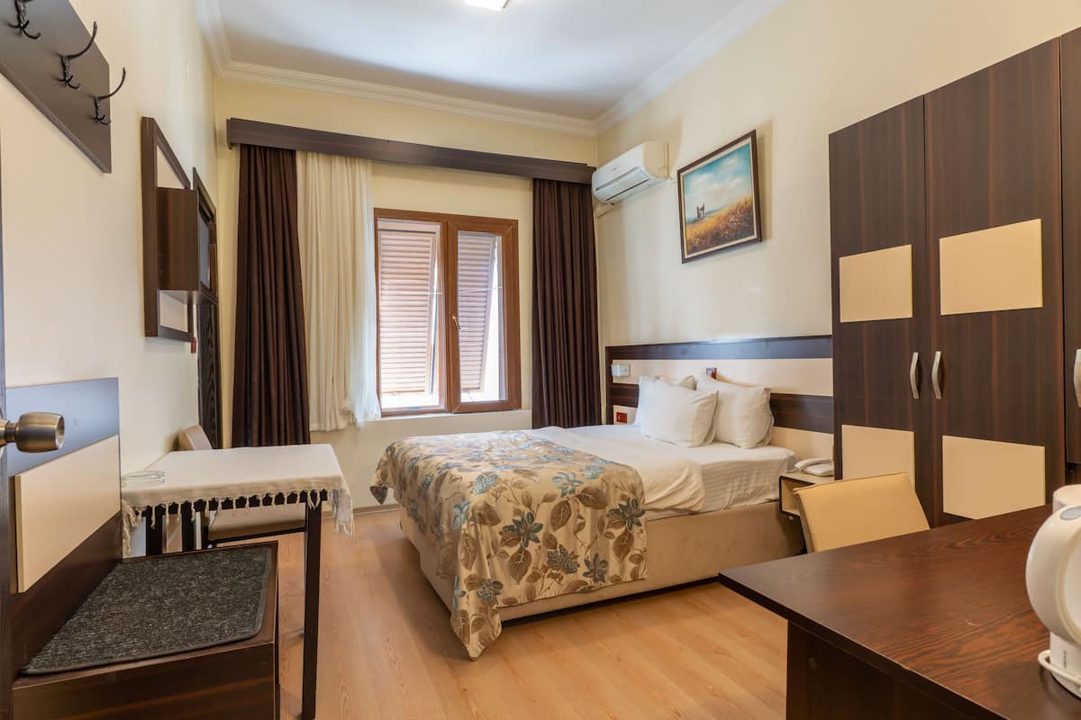 A hotel room with a bed, a desk, a chair, a wardrobe, and a painting on the wall.