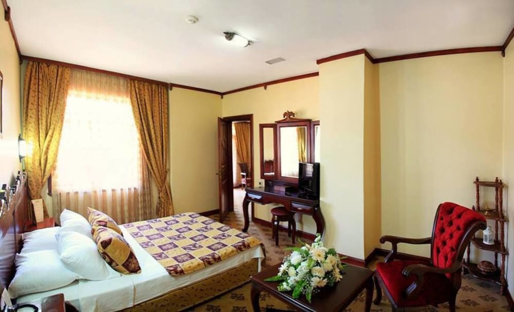 A hotel room with a bed, a desk, a chair, a mirror, and a window with curtains.