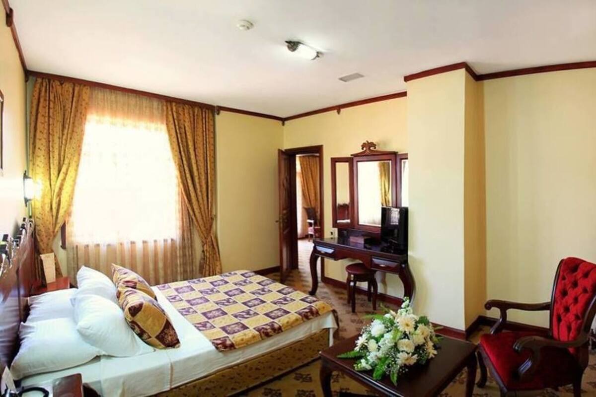 A hotel room with a bed, a desk, a chair, a mirror, and a window with curtains.