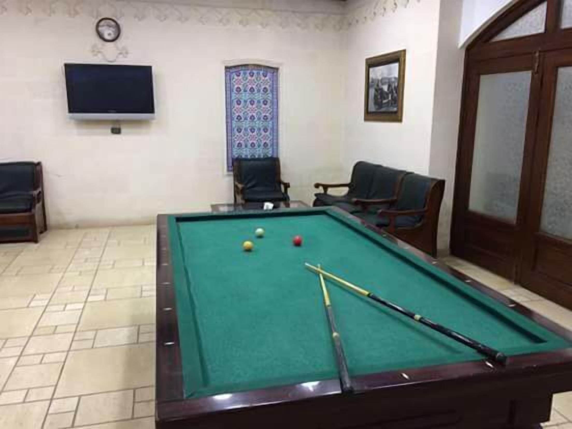 A billiards table with balls and cues, a television, and two chairs in a room with patterned wallpaper and a door with glass panels.