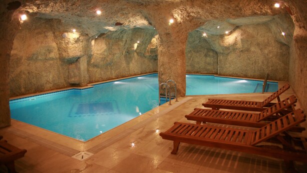 Une piscine intérieure avec des murs en pierre et des chaises longues en bois.