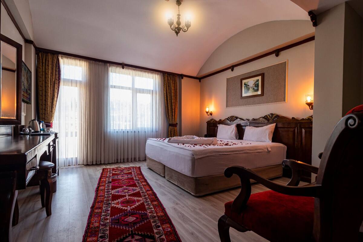 A hotel room with a bed, a desk, a chair, a rug, and a painting on the wall.
