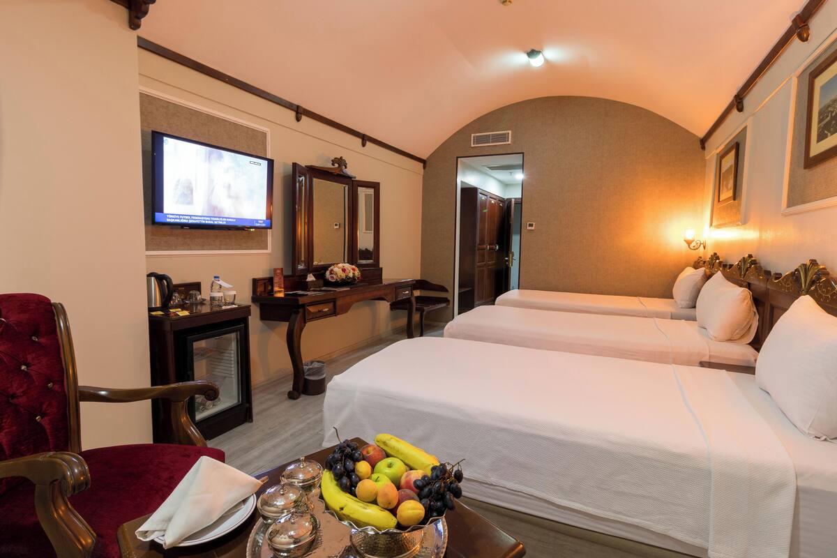 A hotel room with two beds, a TV, a desk, a chair, and a fruit bowl on the nightstand.