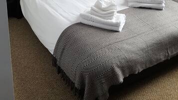 A neatly made bed with white linens and a striped throw blanket, a black nightstand with a lamp, and a power outlet on the wall.