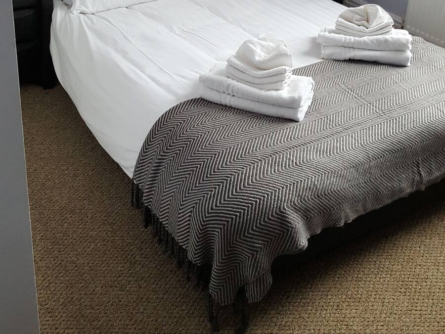A neatly made bed with white linens and a striped throw blanket, a black nightstand with a lamp, and a power outlet on the wall.