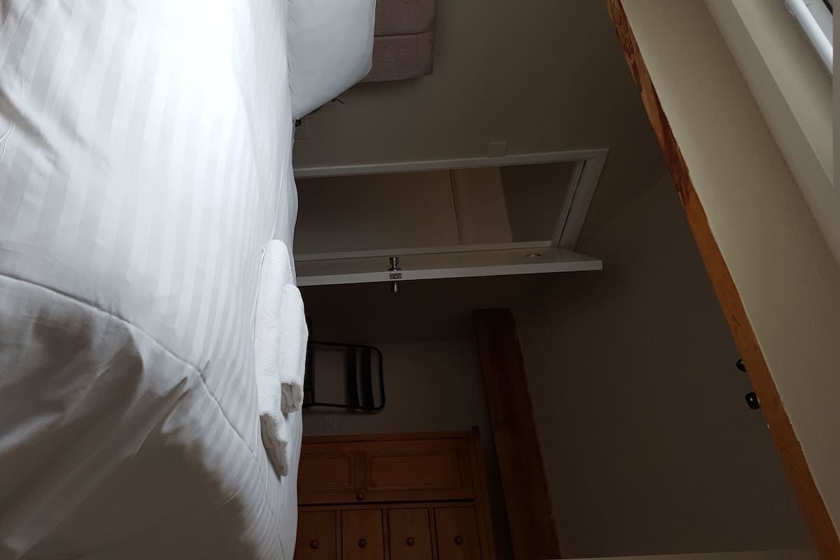 A bedroom with a bunk bed, a wooden wardrobe, and a small window.