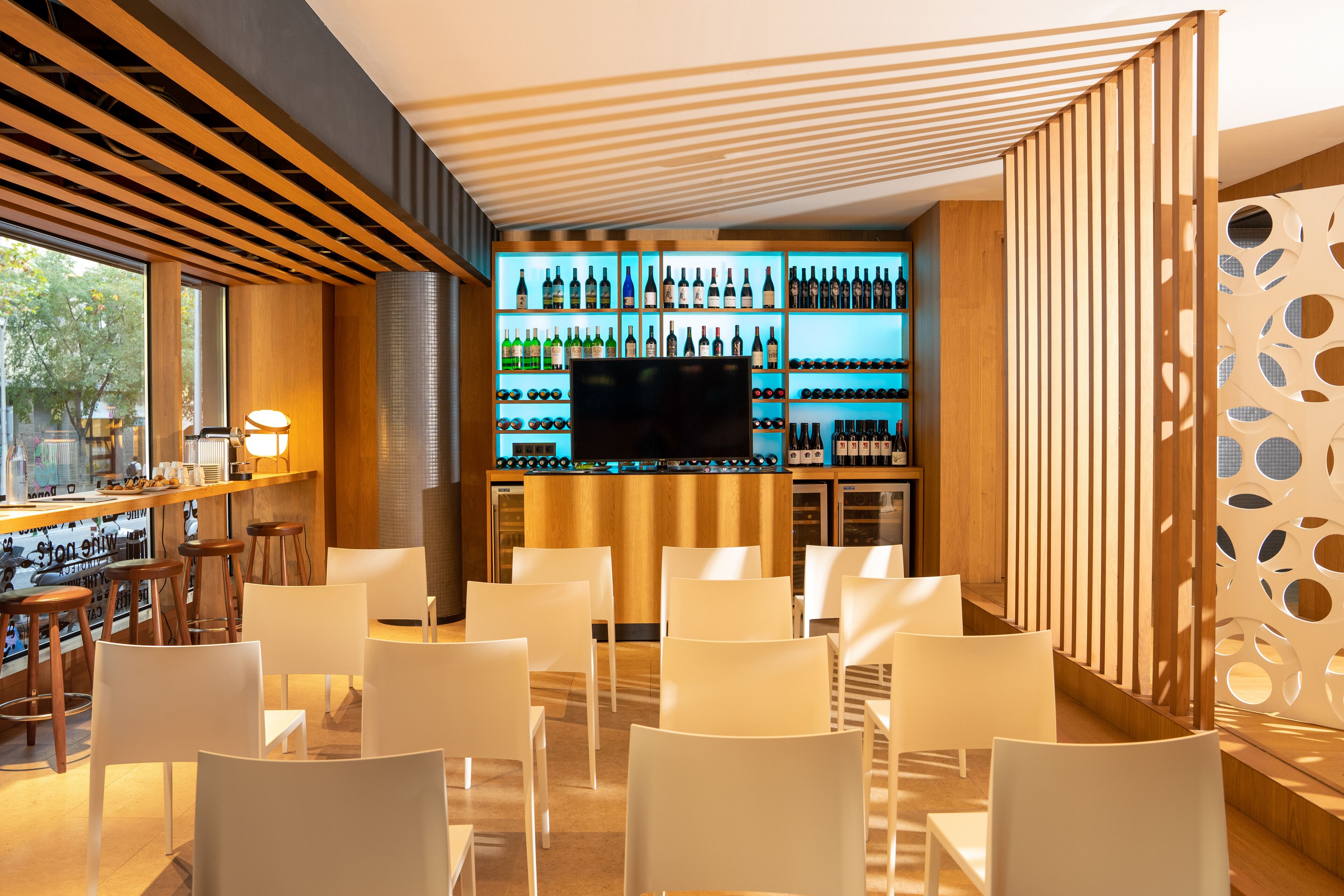 Zona de bar con estantería para vinos, taburetes y pantalla de televisión.