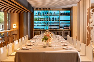 A long dining table set for a meal with a wine rack in the background.