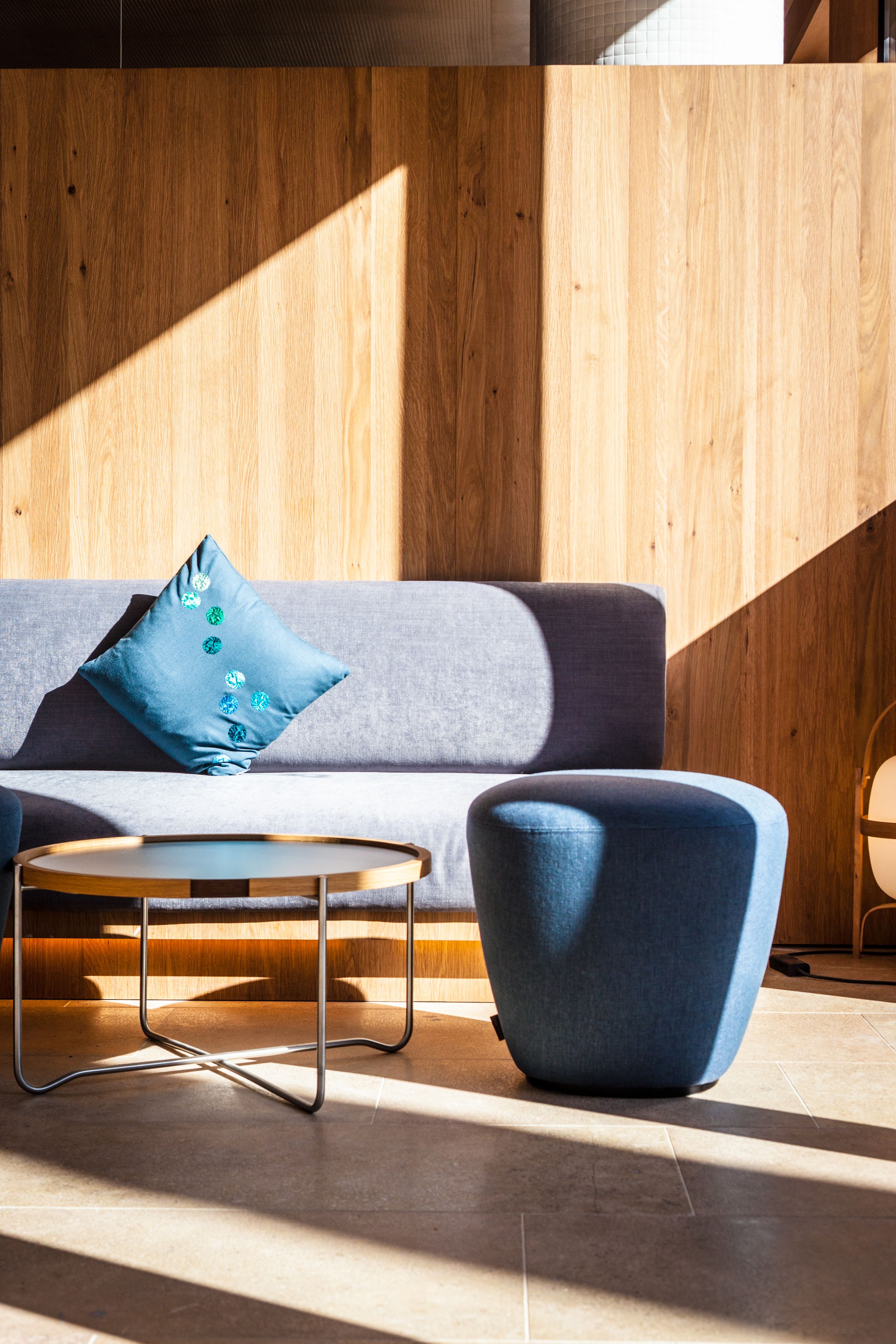 Una sala moderna con un sofá gris, una mesita de centro redonda y un sillón azul.