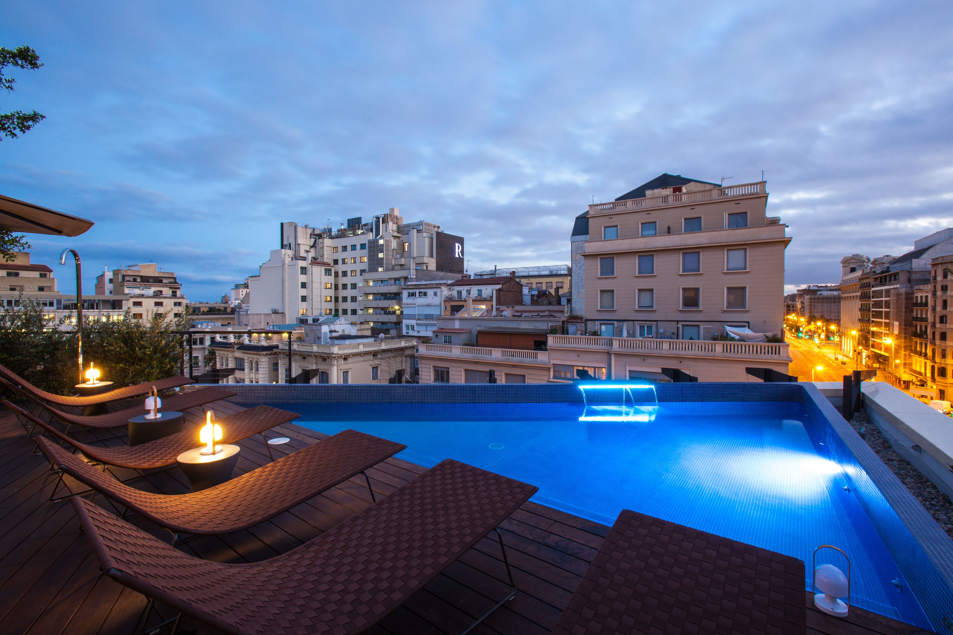 Una piscina en la azotea con sillas de descanso y mesas, rodeada de edificios de la ciudad.