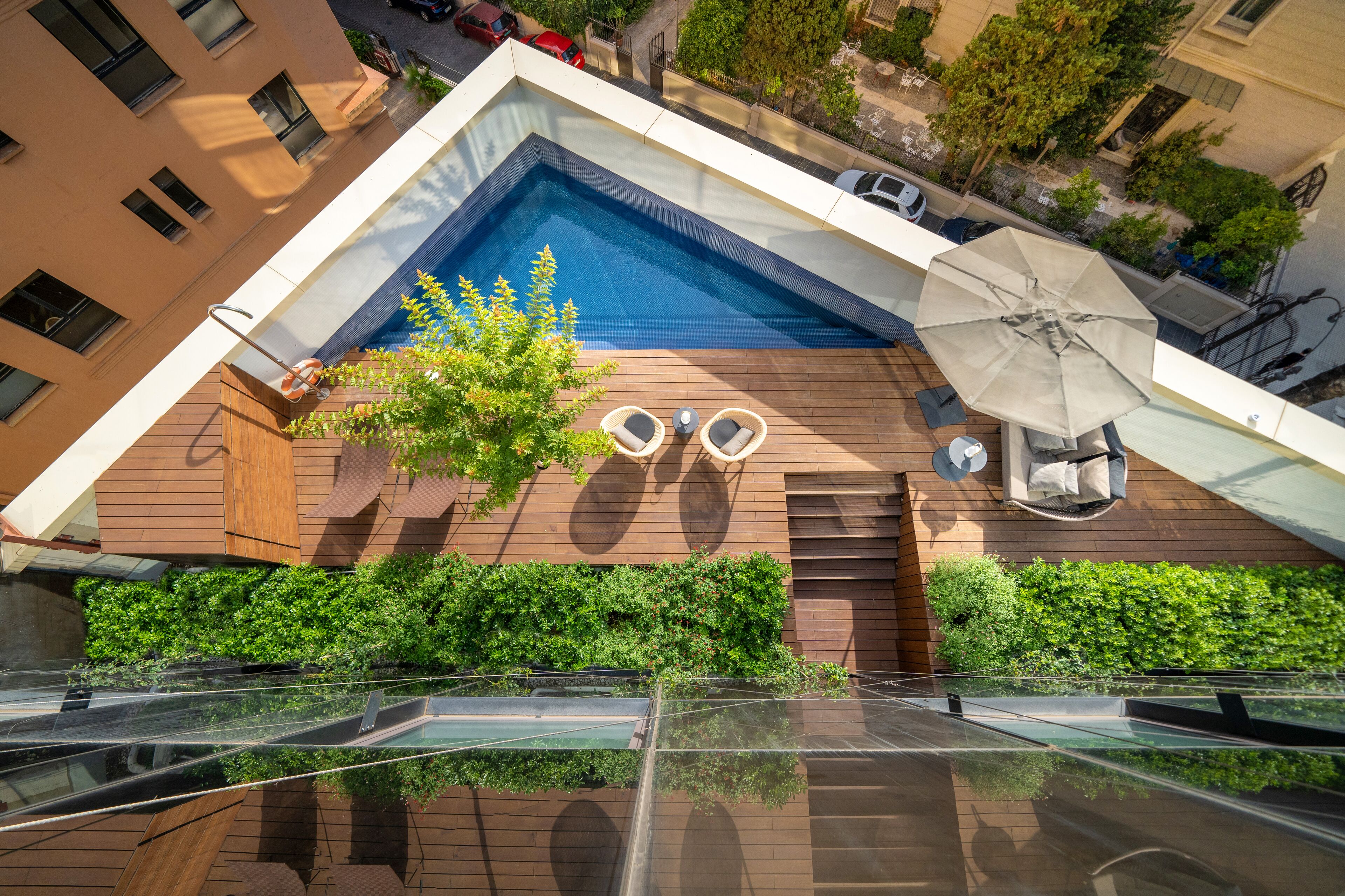 Una piscina en la azotea con terraza de madera, dos sillones de descanso y una sombrilla.