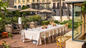 An outdoor dining area with a long table set for a meal, surrounded by wicker chairs and cushioned seating. - Eurostars Barcelona Central (Barcelona)