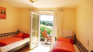 A room with two beds, a chair, and a view of greenery outside. - Landhaus Bettina (Fulda)