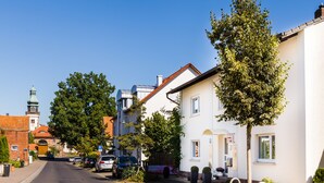 A street view with a white building, parked cars, and a church in the background. - Landhaus Bettina (Fulda)