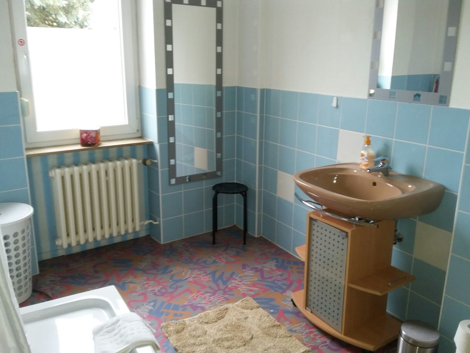 A bathroom with a sink, mirror, radiator, and a window.